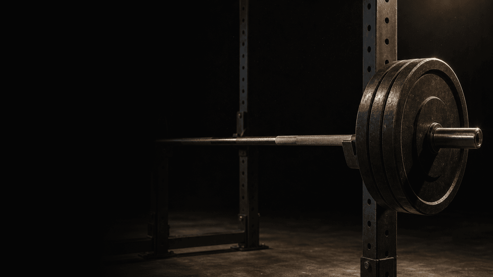 A loaded barbell resting on a squat rack in a dark gym, lit from one side